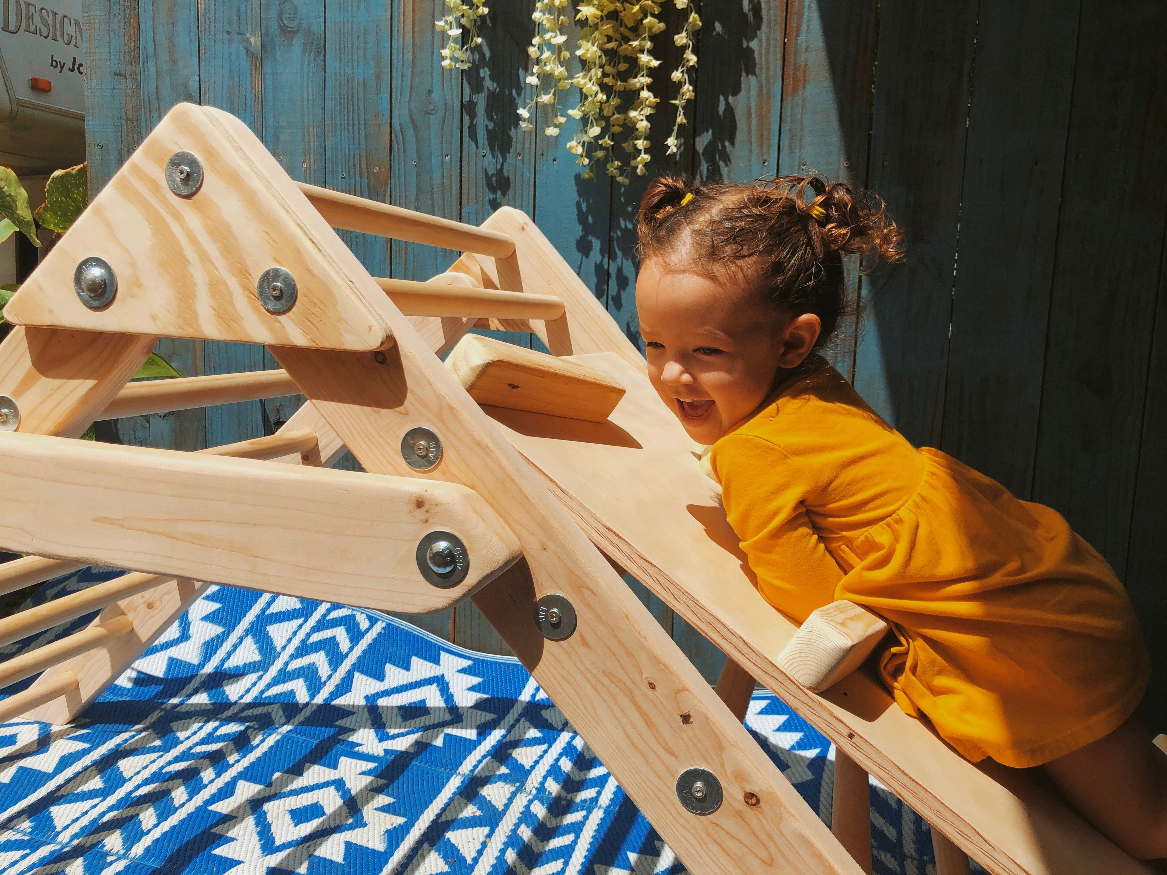 Toddler plays happily on wooden triangle climber outdoors